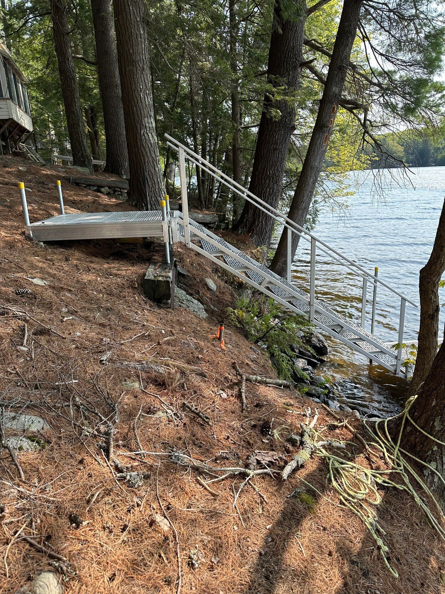 Wooded lakeshore with a small wooden dock and metal railing beside the water