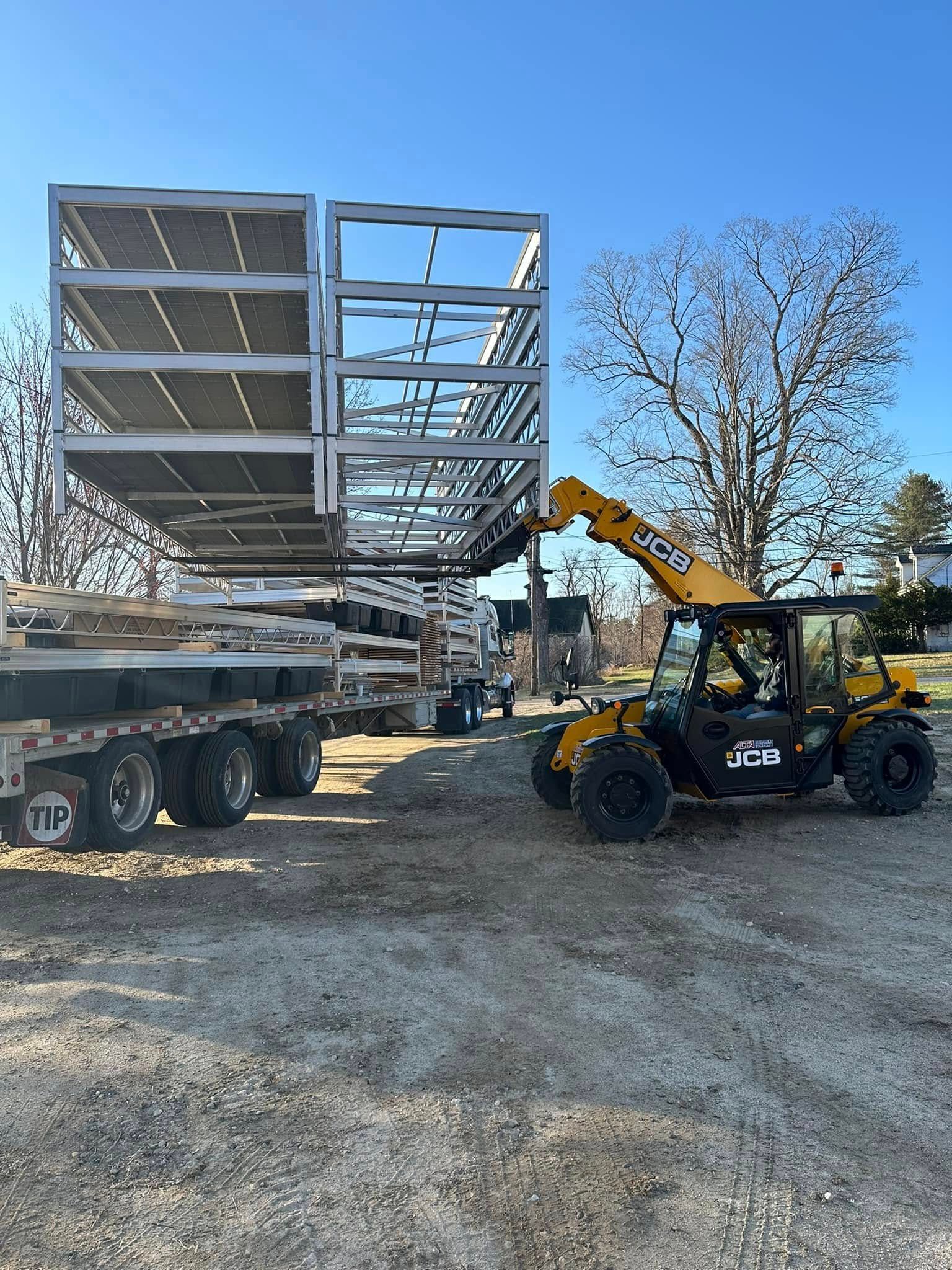 Yellow forklift lifting a steel structure on a flatbed trailer at a gravel construction site.