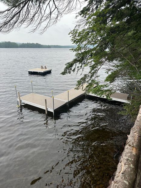 Dock jutting into a gray lake with a small boat nearby and trees overhanging the shore