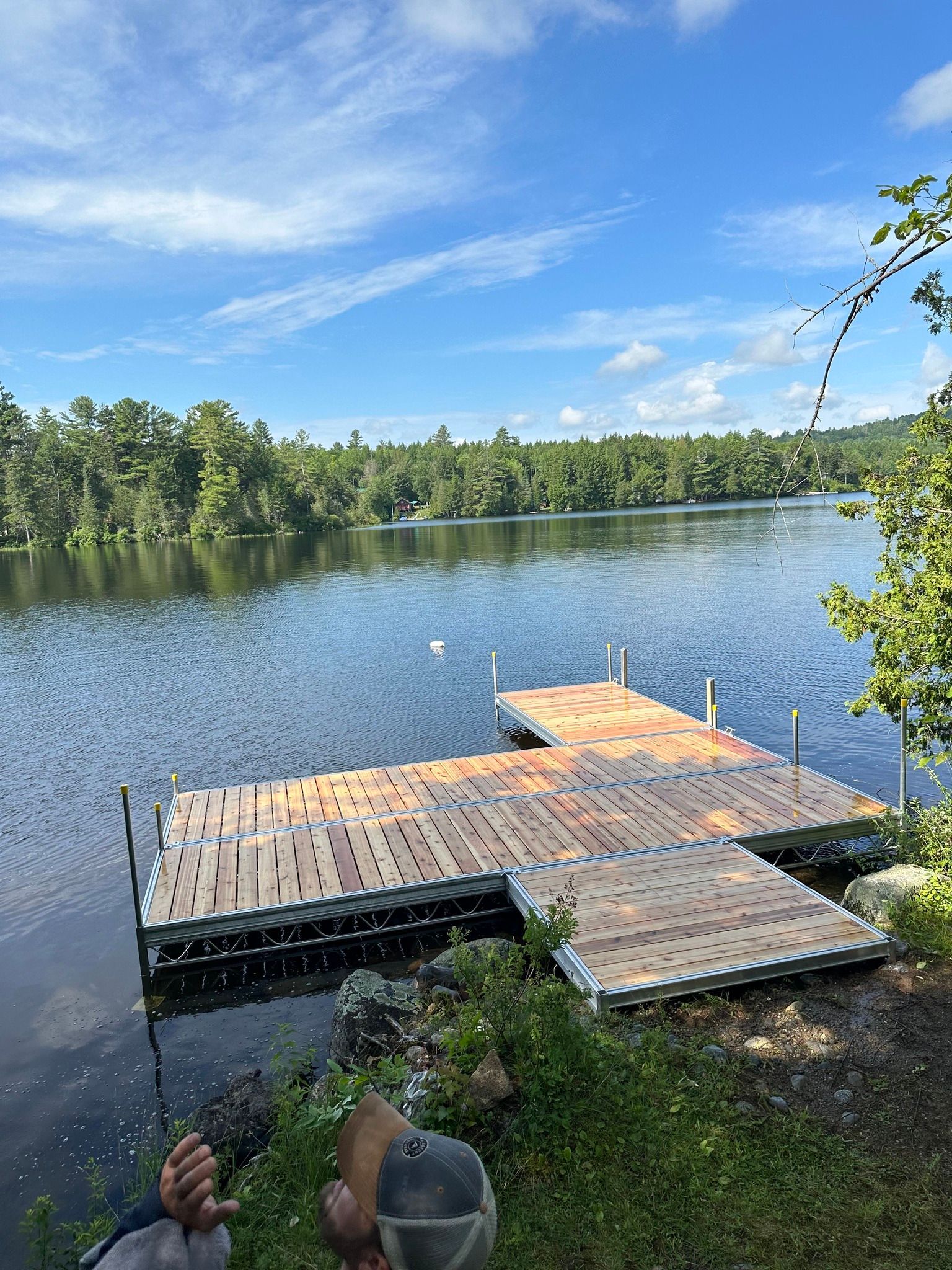 Wooden dock extending into a calm lake under a blue sky, with trees lining the shore.