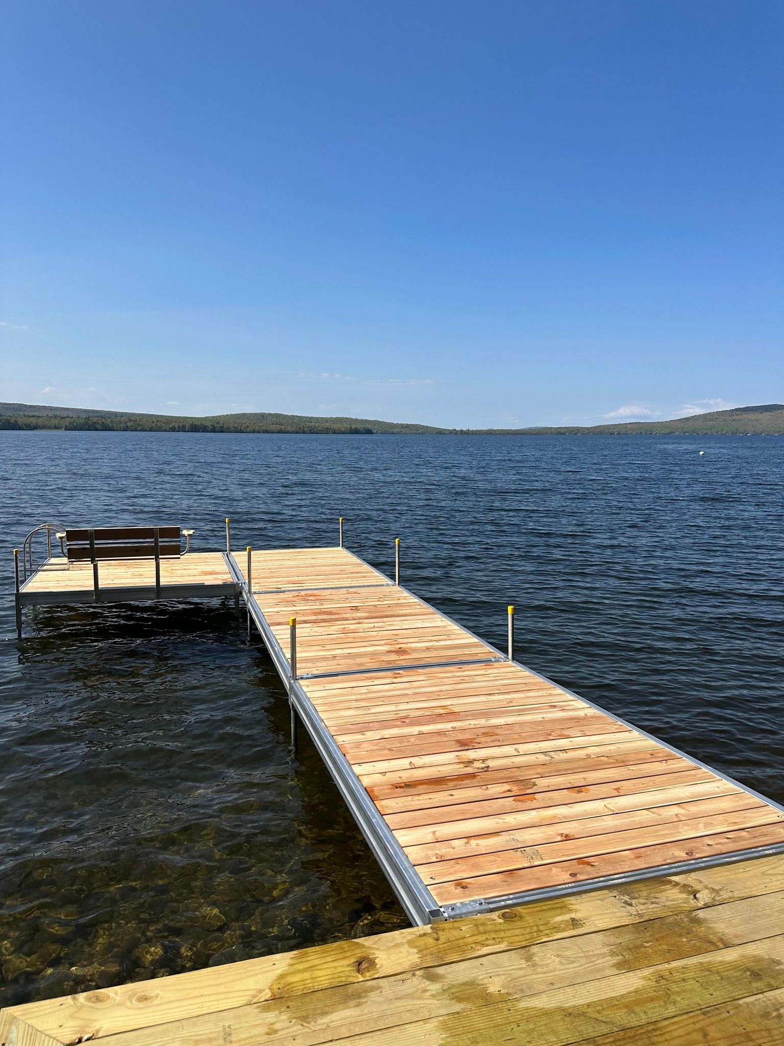 Wooden dock extending into a calm lake under a clear blue sky