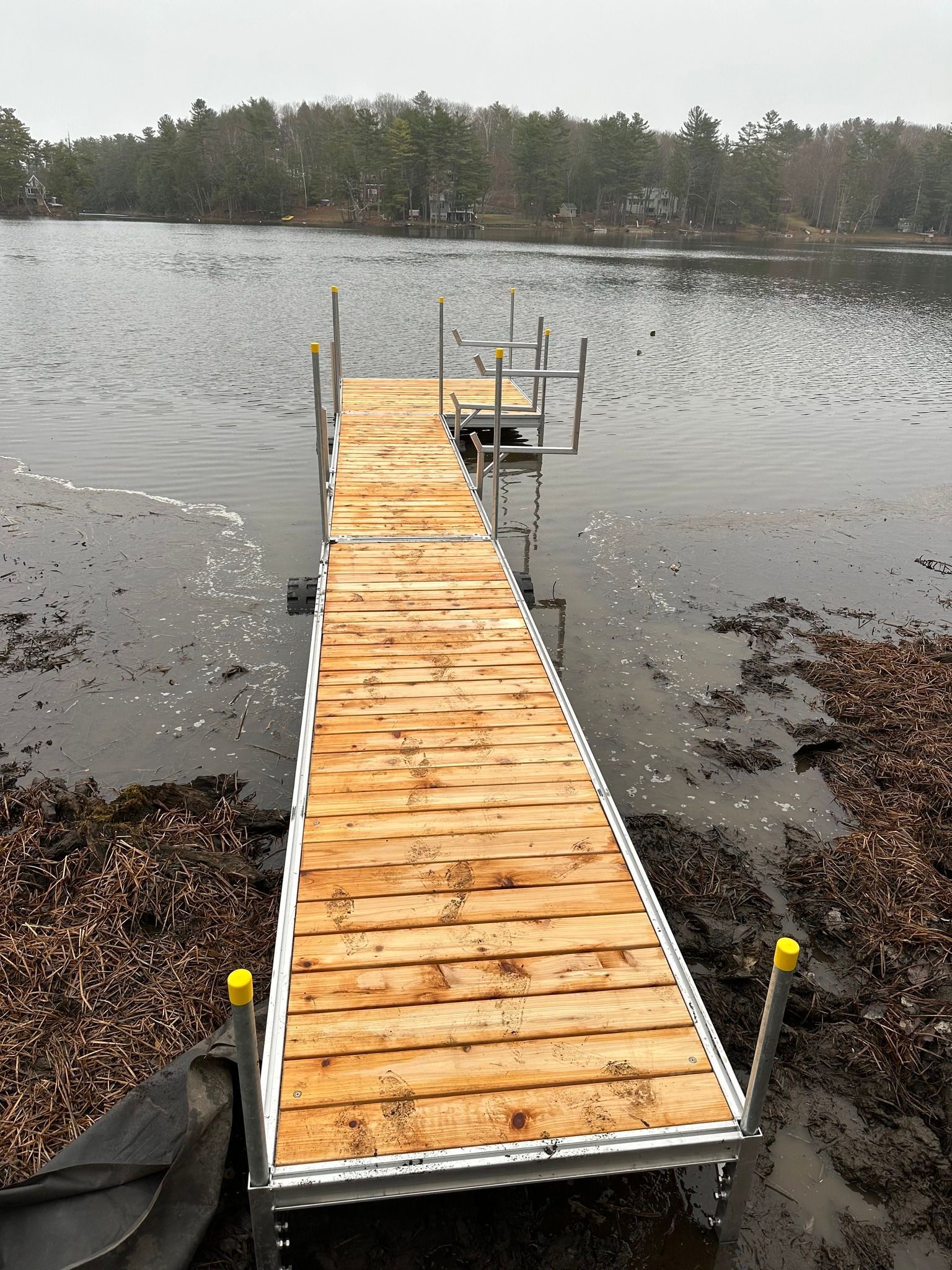 Wooden dock extending into a calm lake, with a forested shoreline in the background.