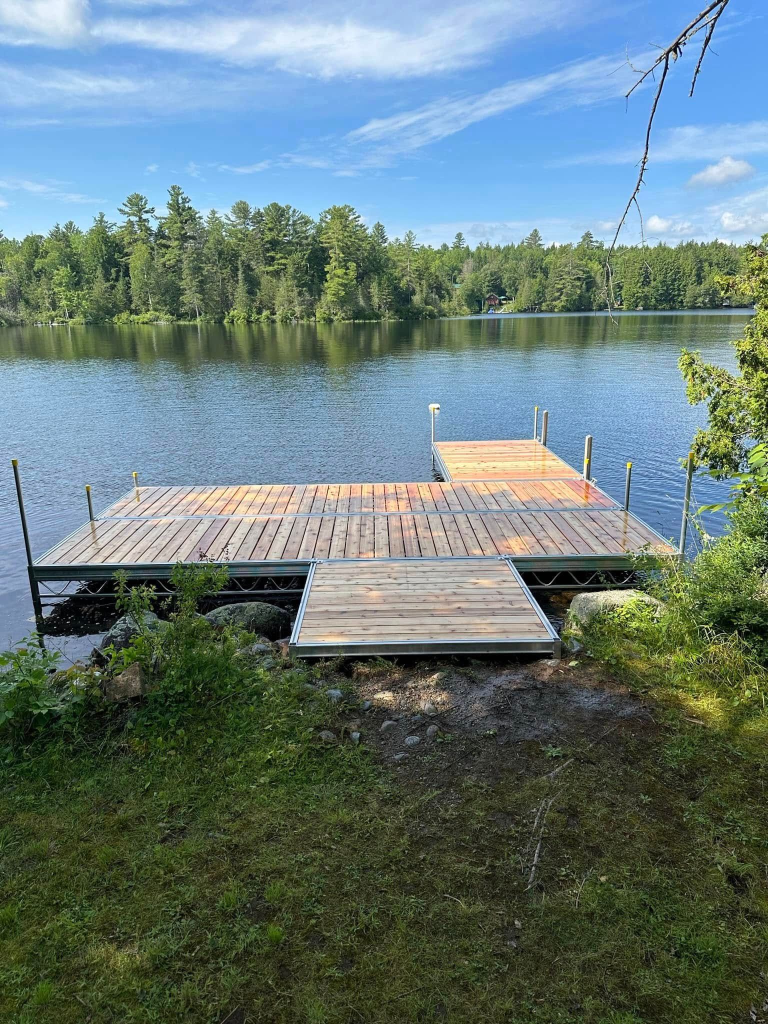 Wooden dock extending into a calm lake, with a forested shoreline and clear blue sky.