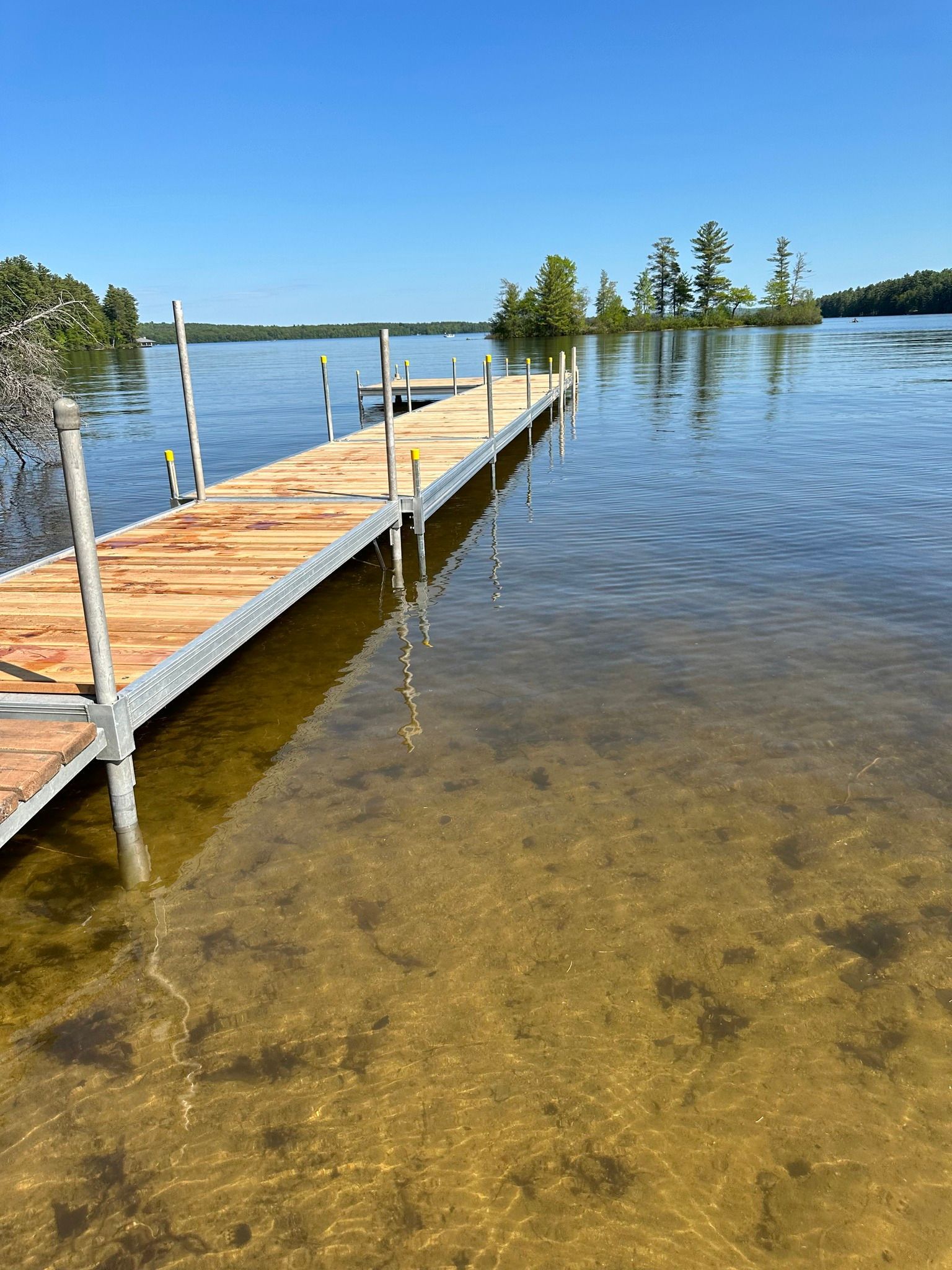 Wooden dock extending into clear, shallow lake water under a bright blue sky