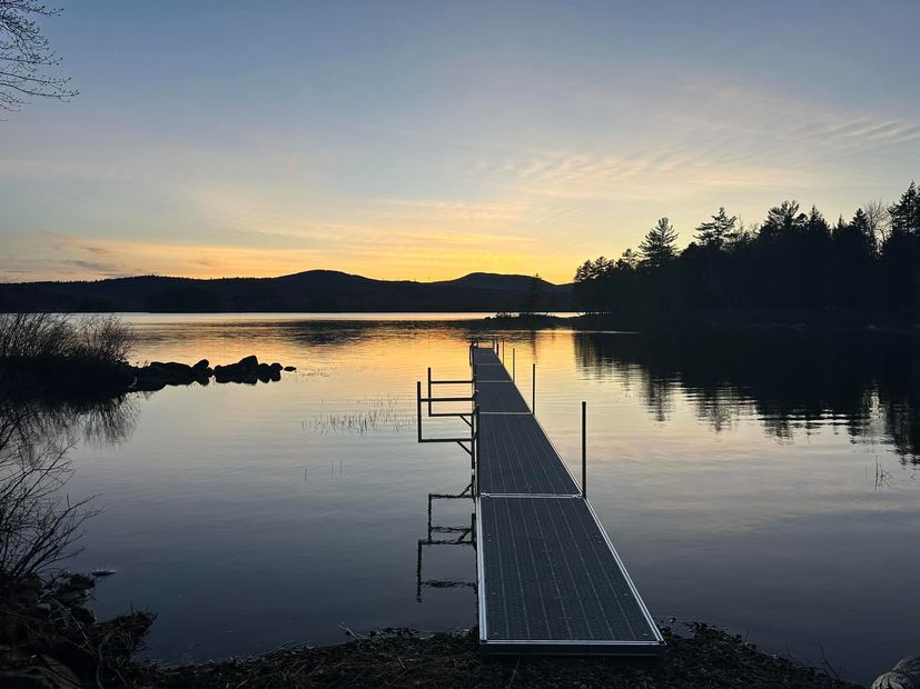 Sunset over a calm lake with a dock leading into the water and silhouetted trees on the shore