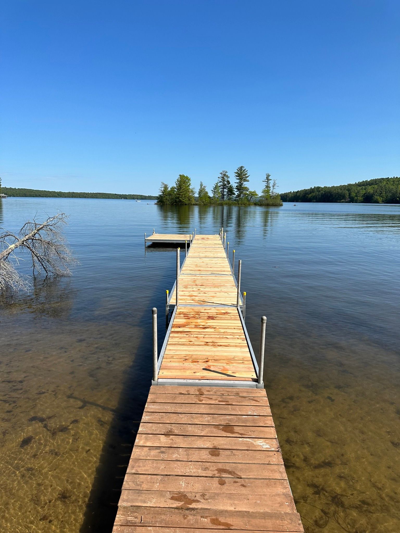 Wooden dock extending into a calm lake under a clear blue sky.