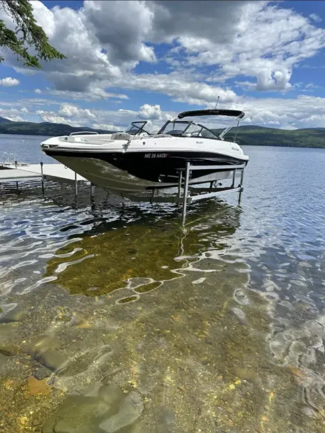 White motorboat on a lift in shallow lake water under a cloudy sky, with mountains in the distance