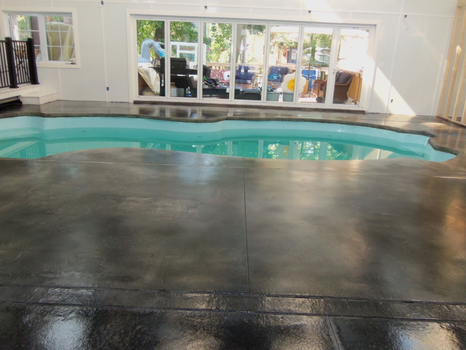 Indoor pool with dark concrete floor and large sliding glass doors leading outside.