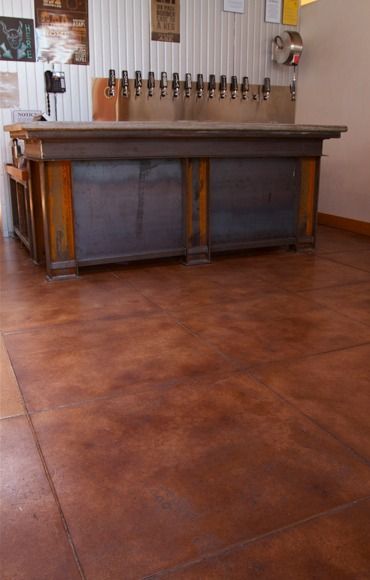 Wooden bar with beer taps against a white wall. Brown stained concrete floor.