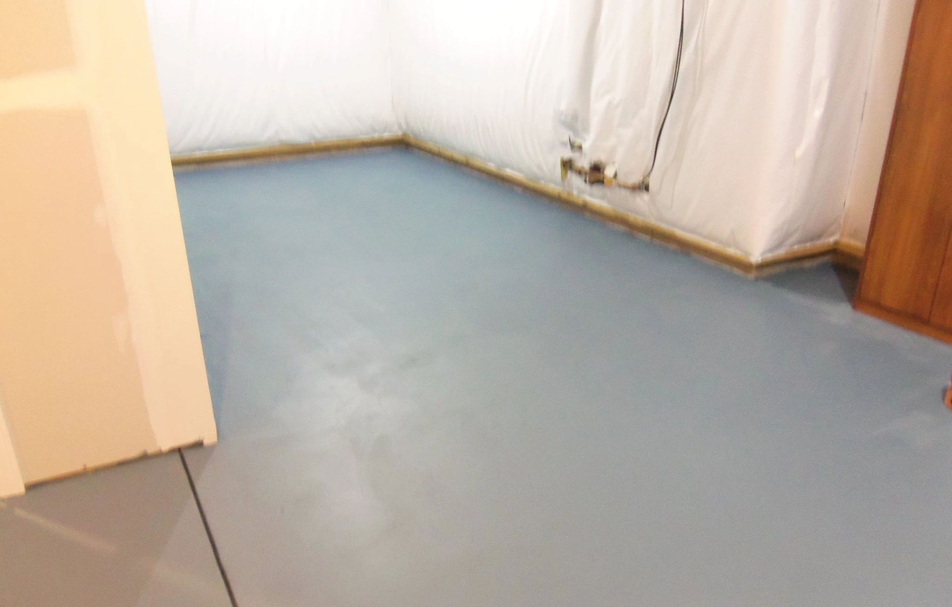 Blue painted basement floor with white walls and a wooden door.