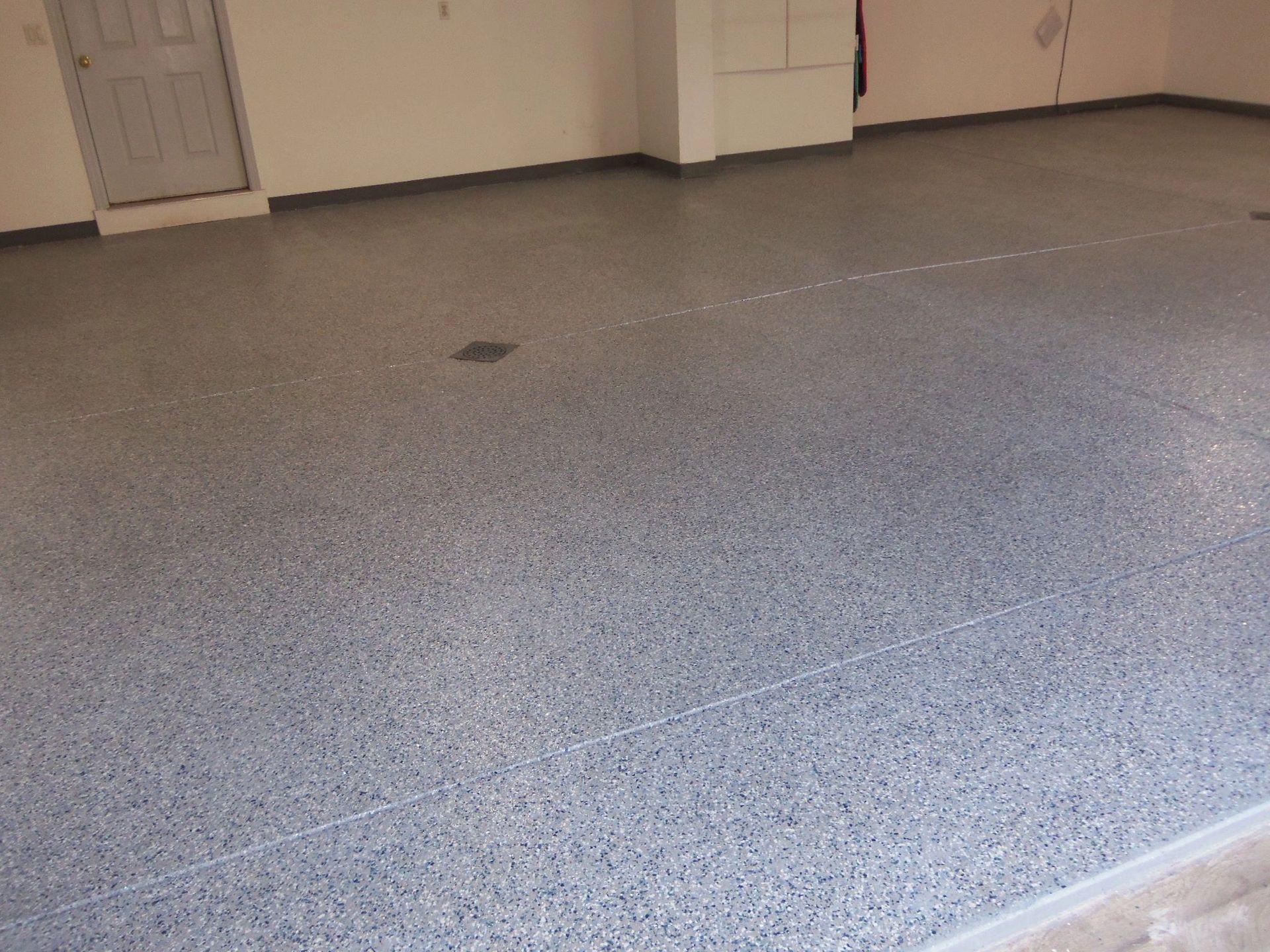 Gray speckled epoxy floor in a garage with a door, and white walls.