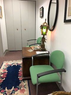 A waiting room with green chairs , a desk , a lamp and a mirror.