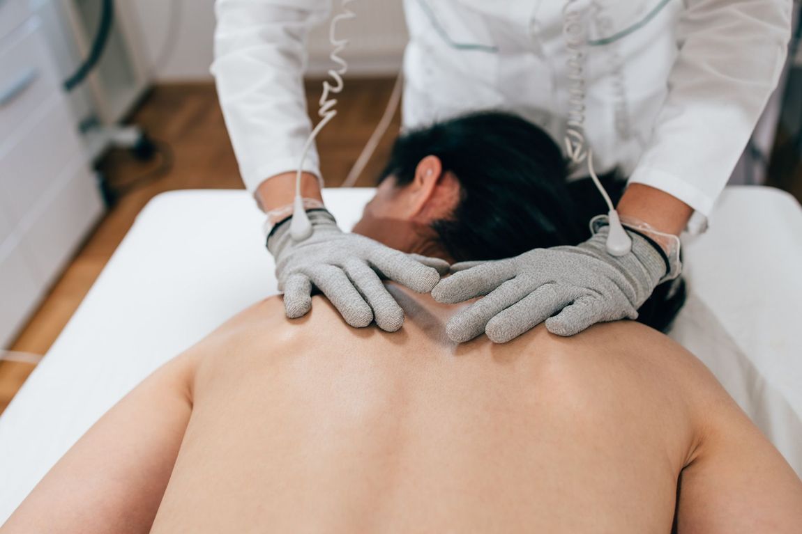 A woman is laying on a bed getting a bio-electric massage from a doctor.