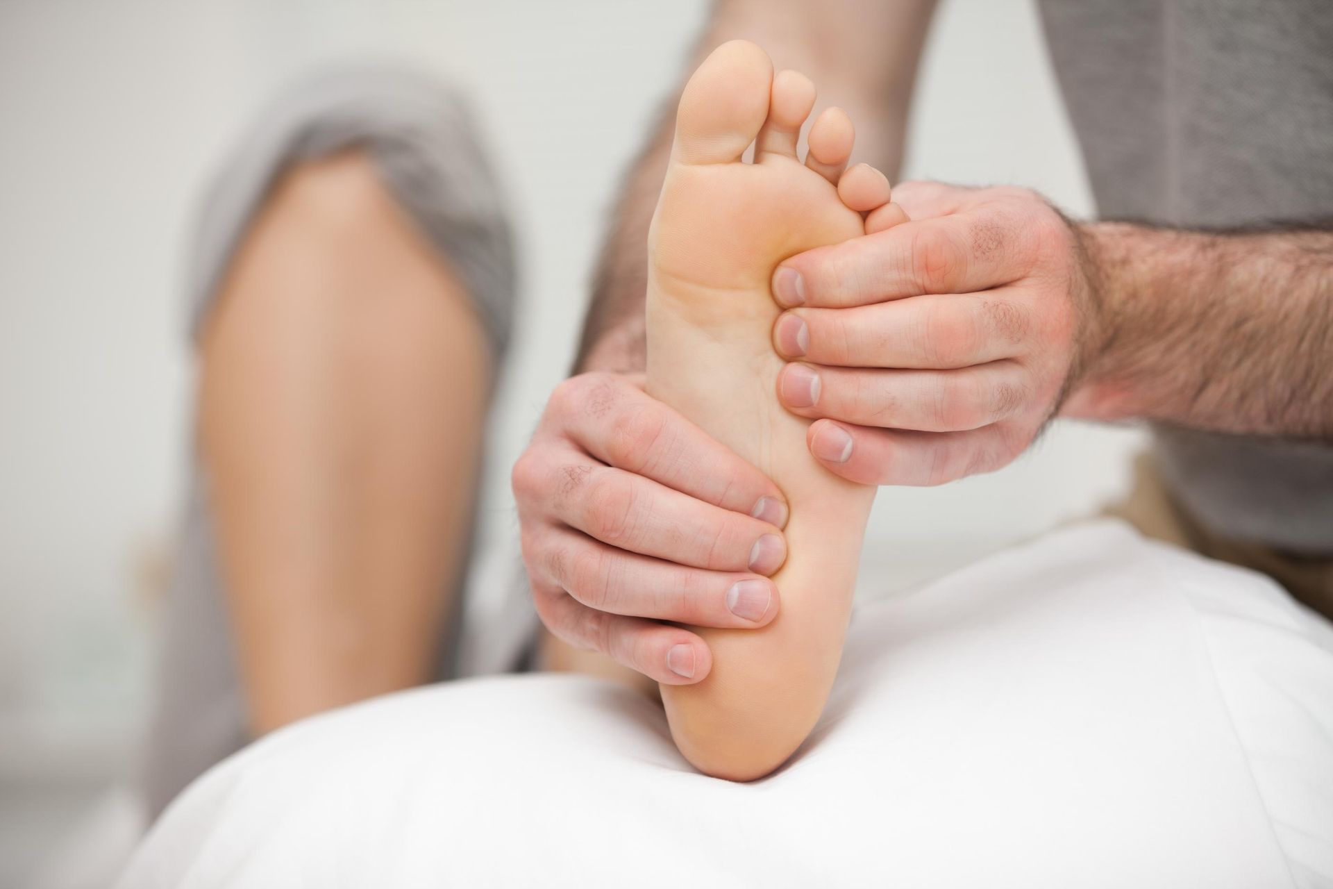 Hands massaging the sole of a bare foot on a white treatment table