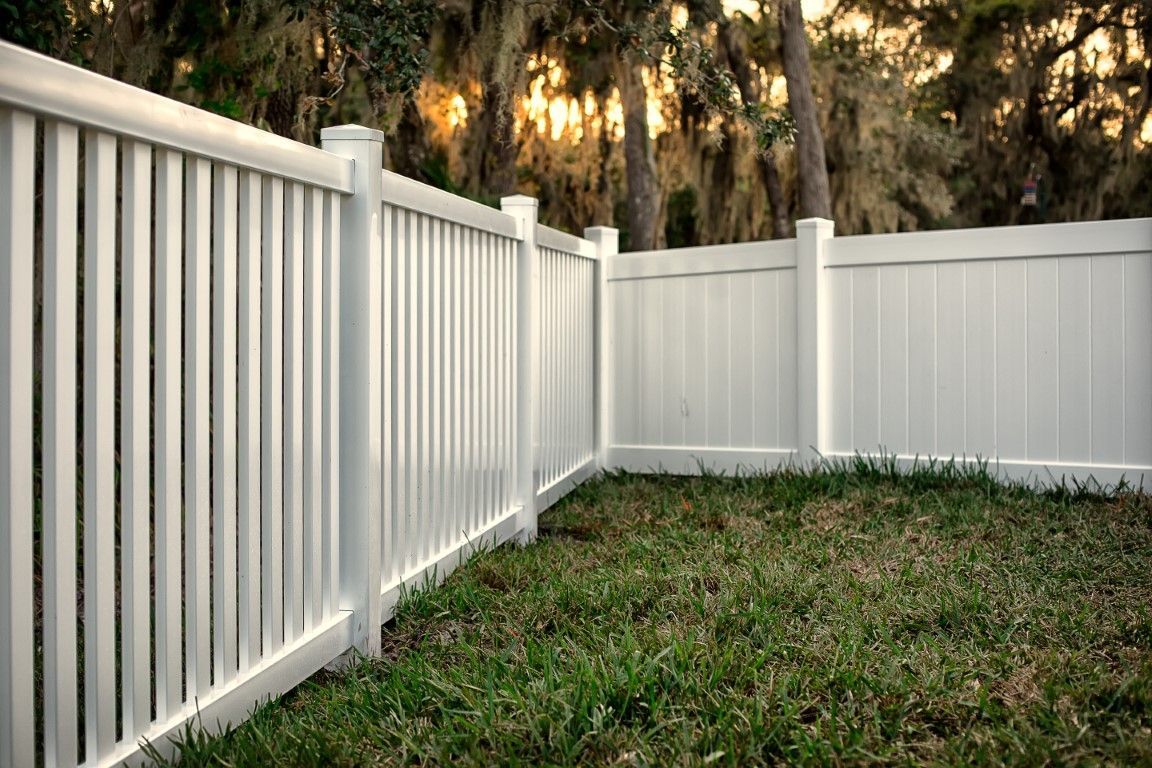 White vinyl fence bordering a grassy yard beside trees and a wooded area