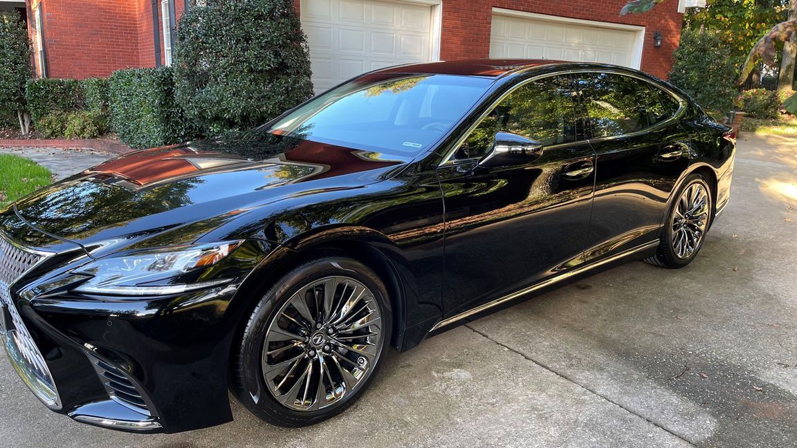 A black lexus ls 500 is parked in a driveway in front of a house.