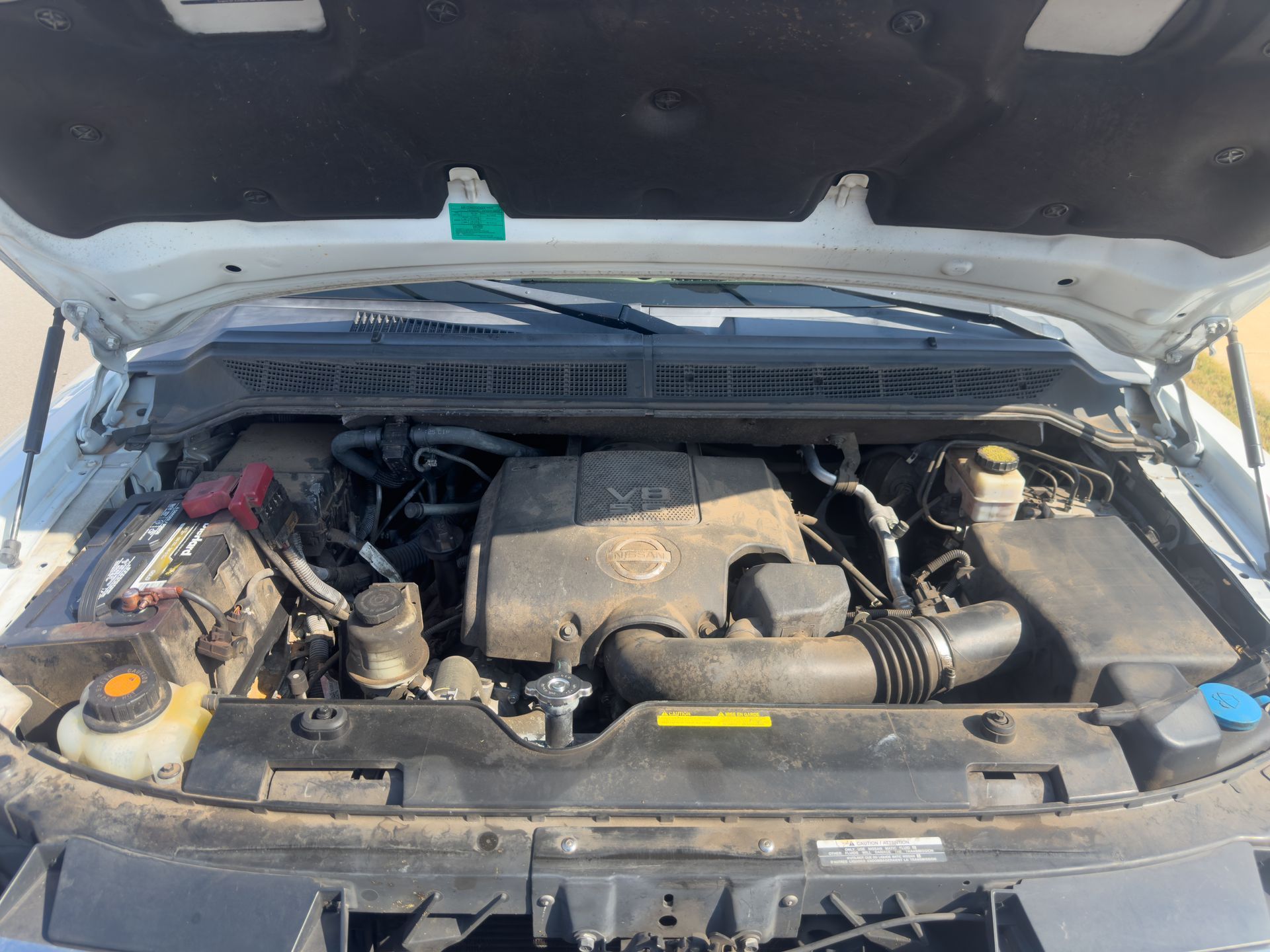 Open car hood showing a dusty engine compartment and visible fluid reservoirs