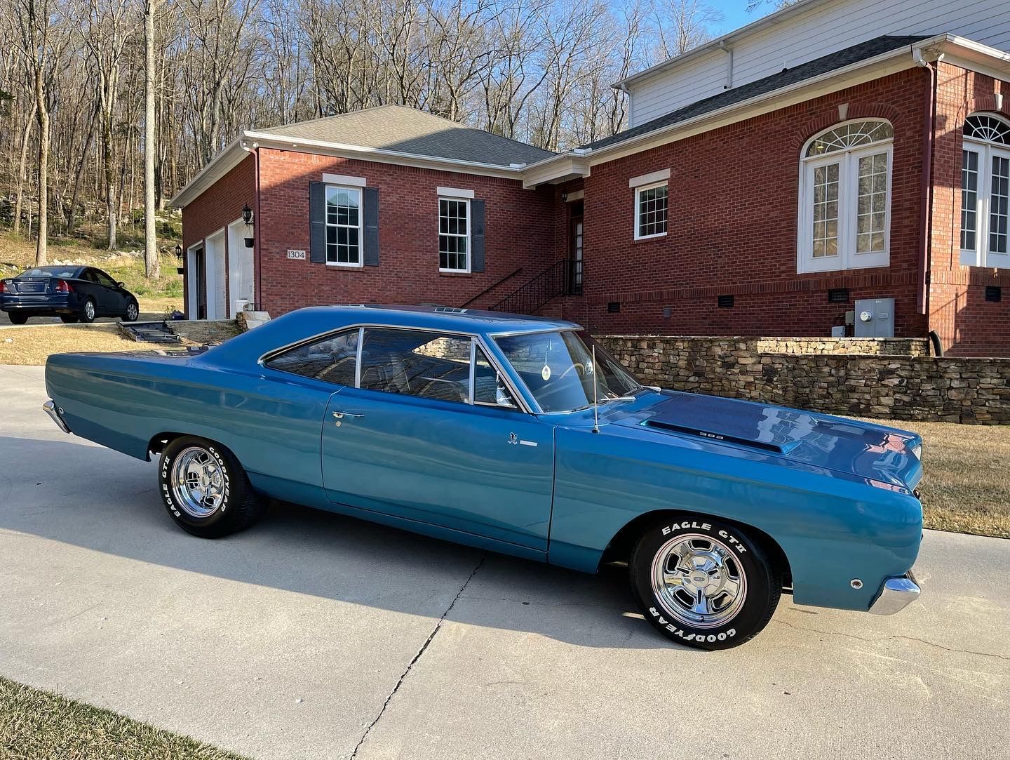A blue car is parked in front of a brick house.
