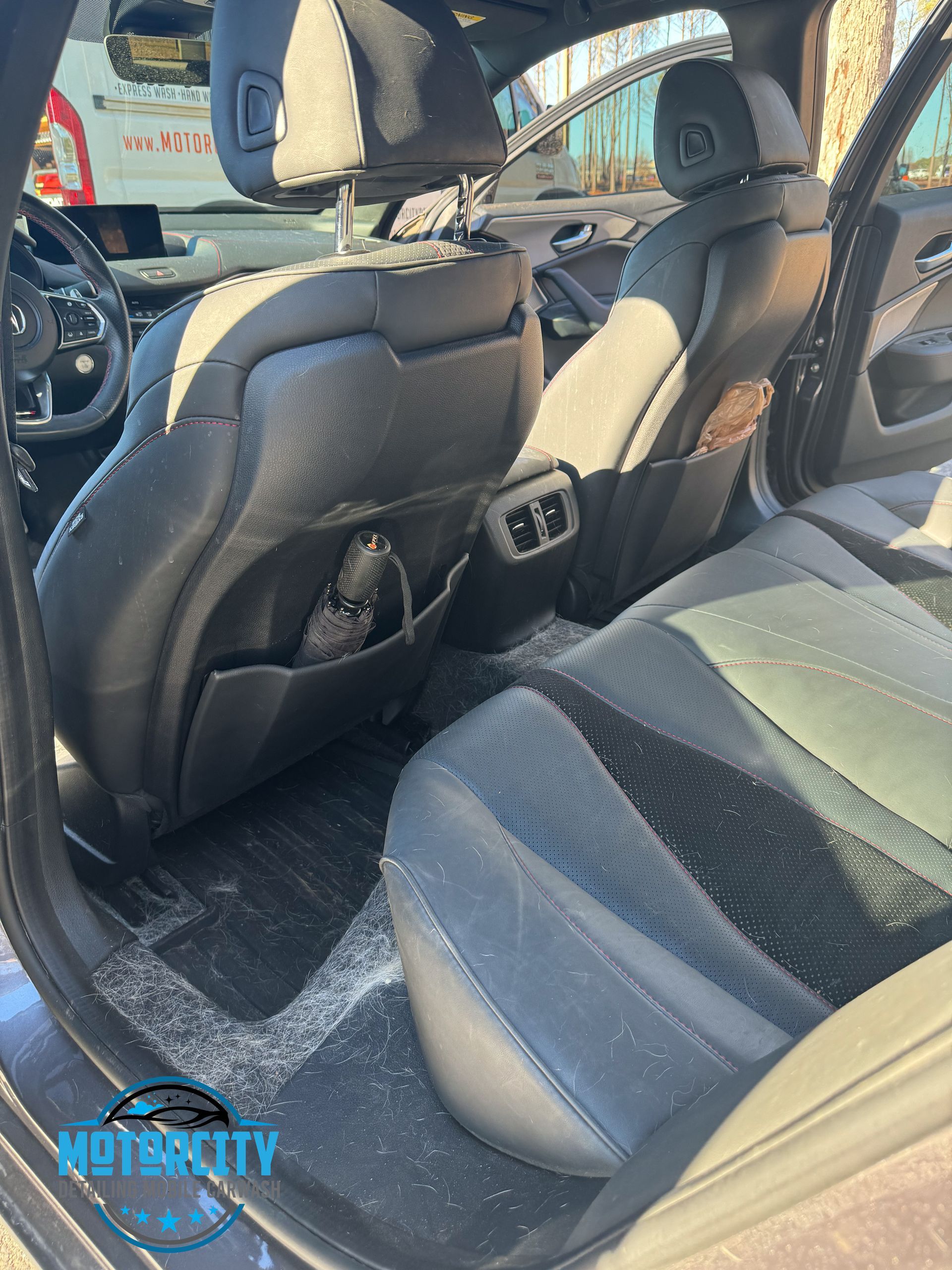 Car interior with black leather seats and folded rear seatback, viewed from the open rear door