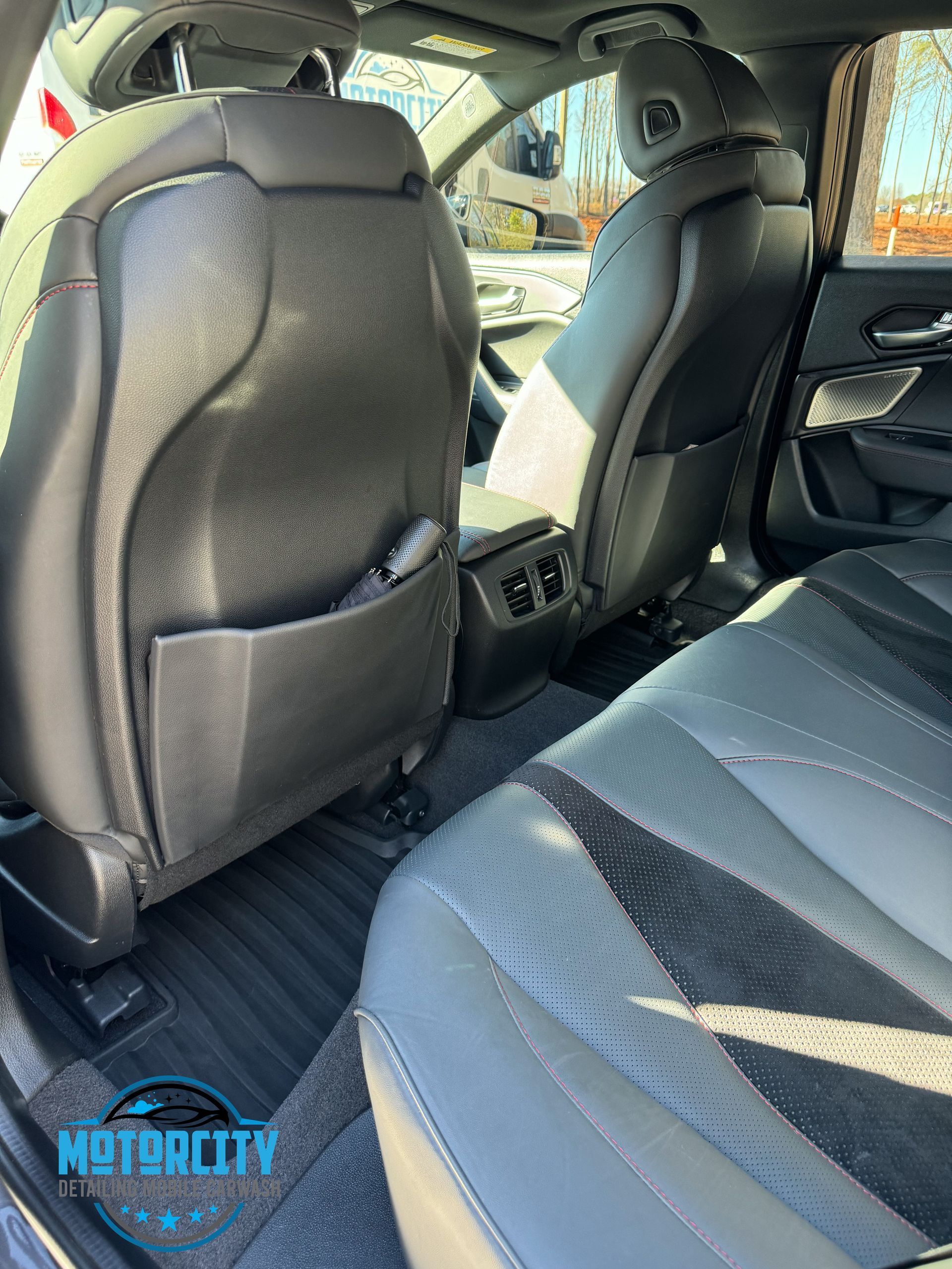 Car interior with black leather seats and rear floor mat, viewed from the back seat.