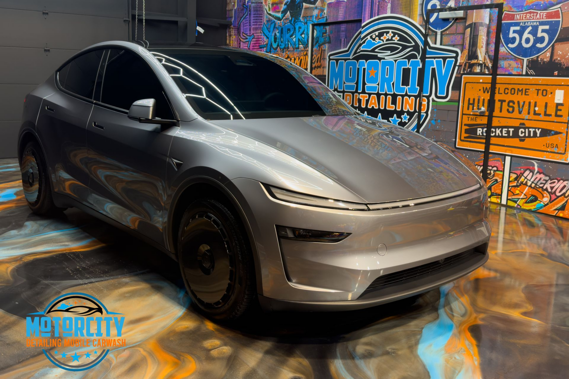 Gray Tesla Model Y car in front of a colorful graffiti wall.