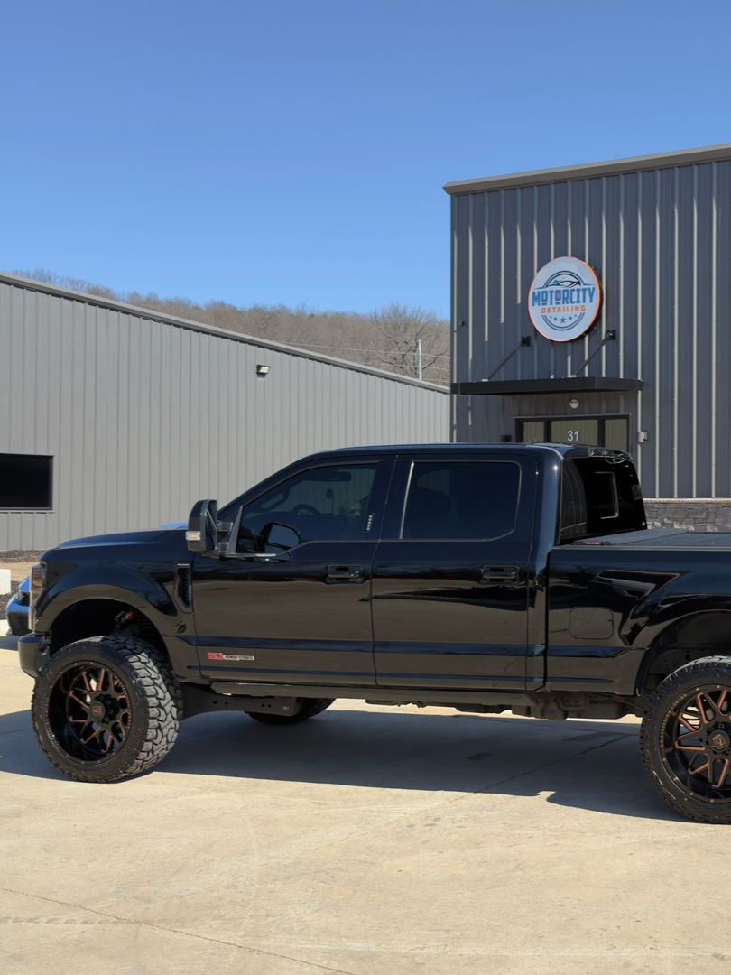 Black pickup truck parked outside a metal workshop with an open garage door.