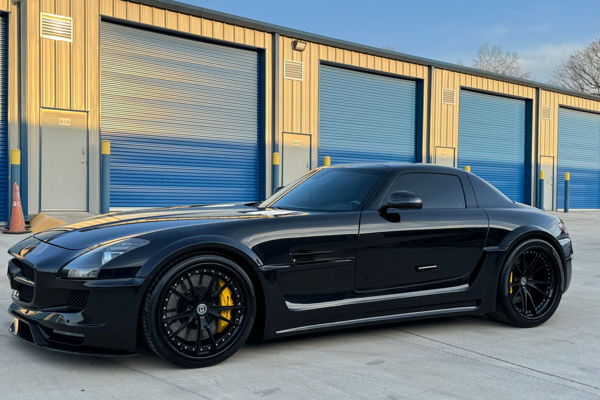 A black sports car is parked in front of a building with blue garage doors.