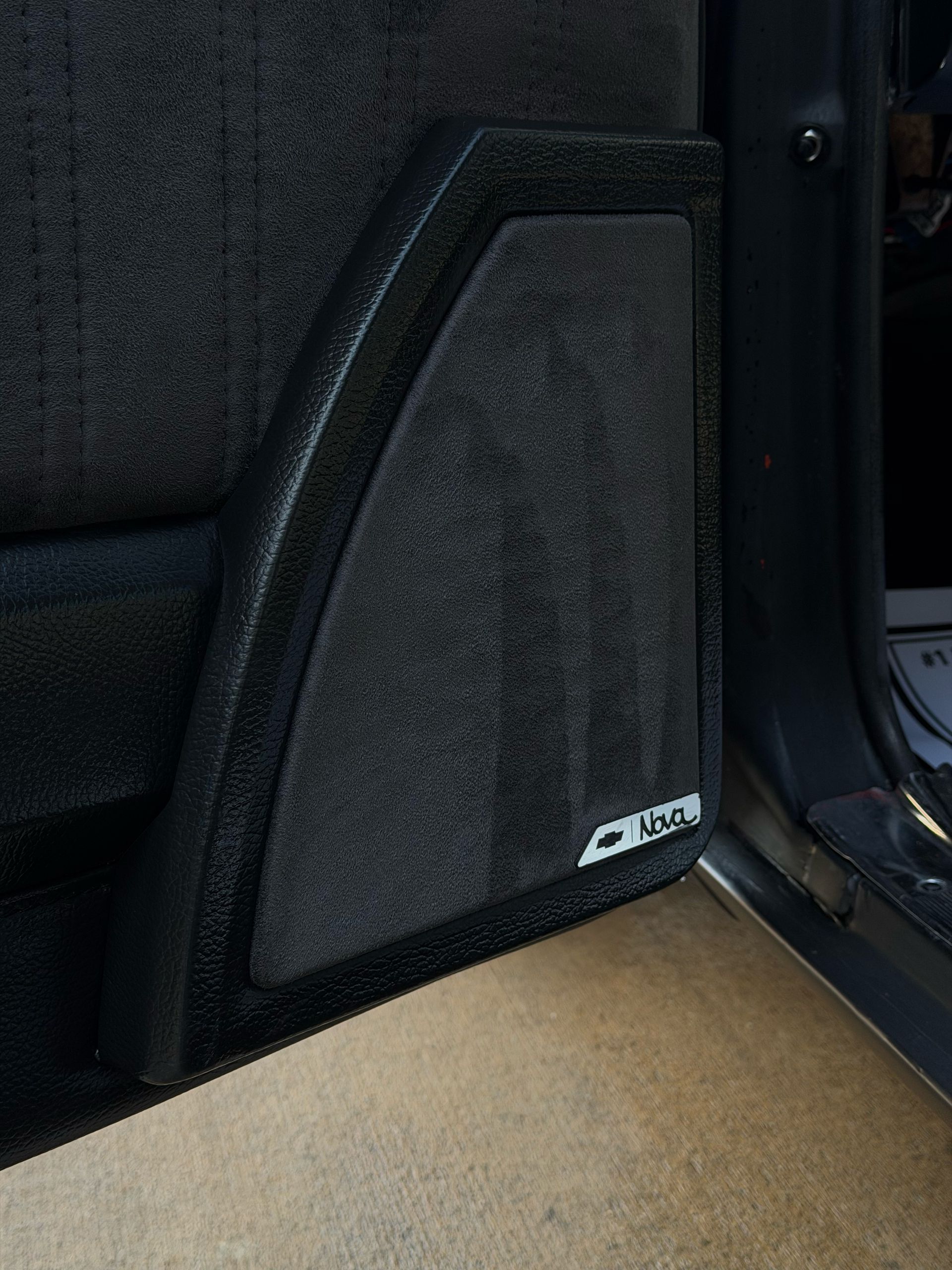 Car trunk side panel with black speaker enclosure and tan carpeted floor mat.
