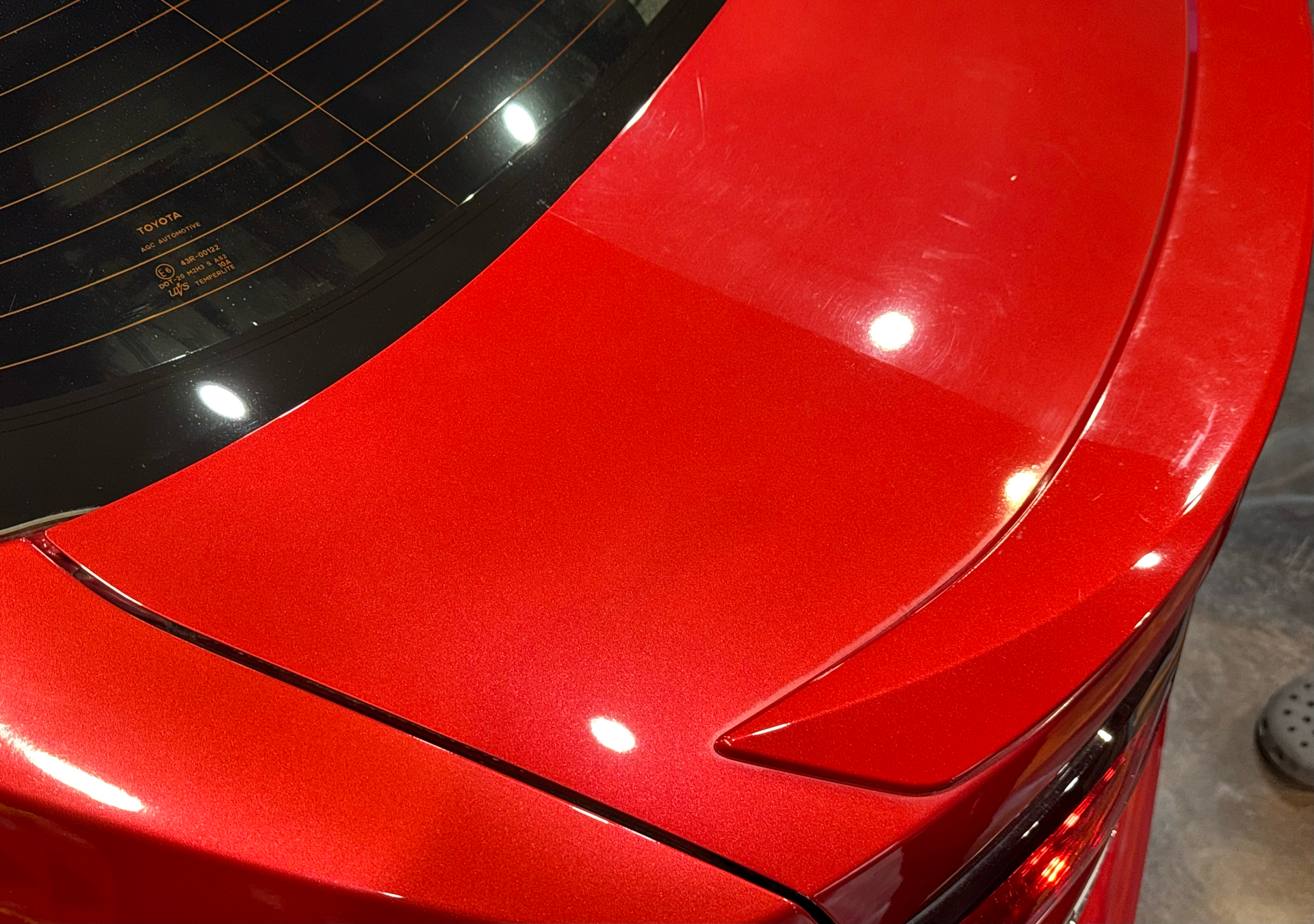 Red car trunk and spoiler with shiny paint; a window is in the background.