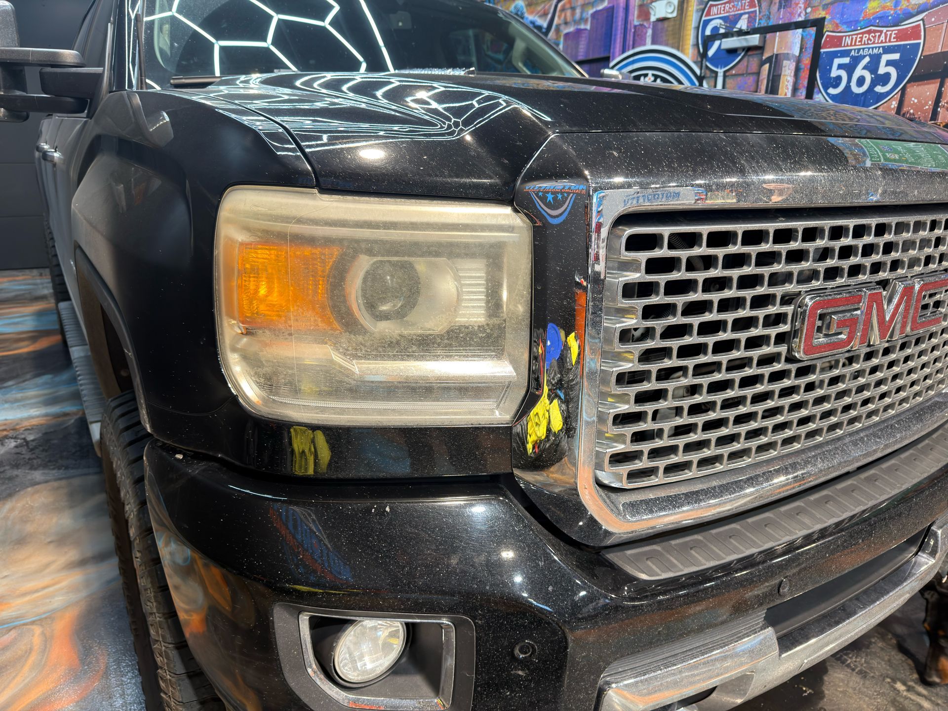 Close-up of a black GMC truck front grille and headlight inside a shop