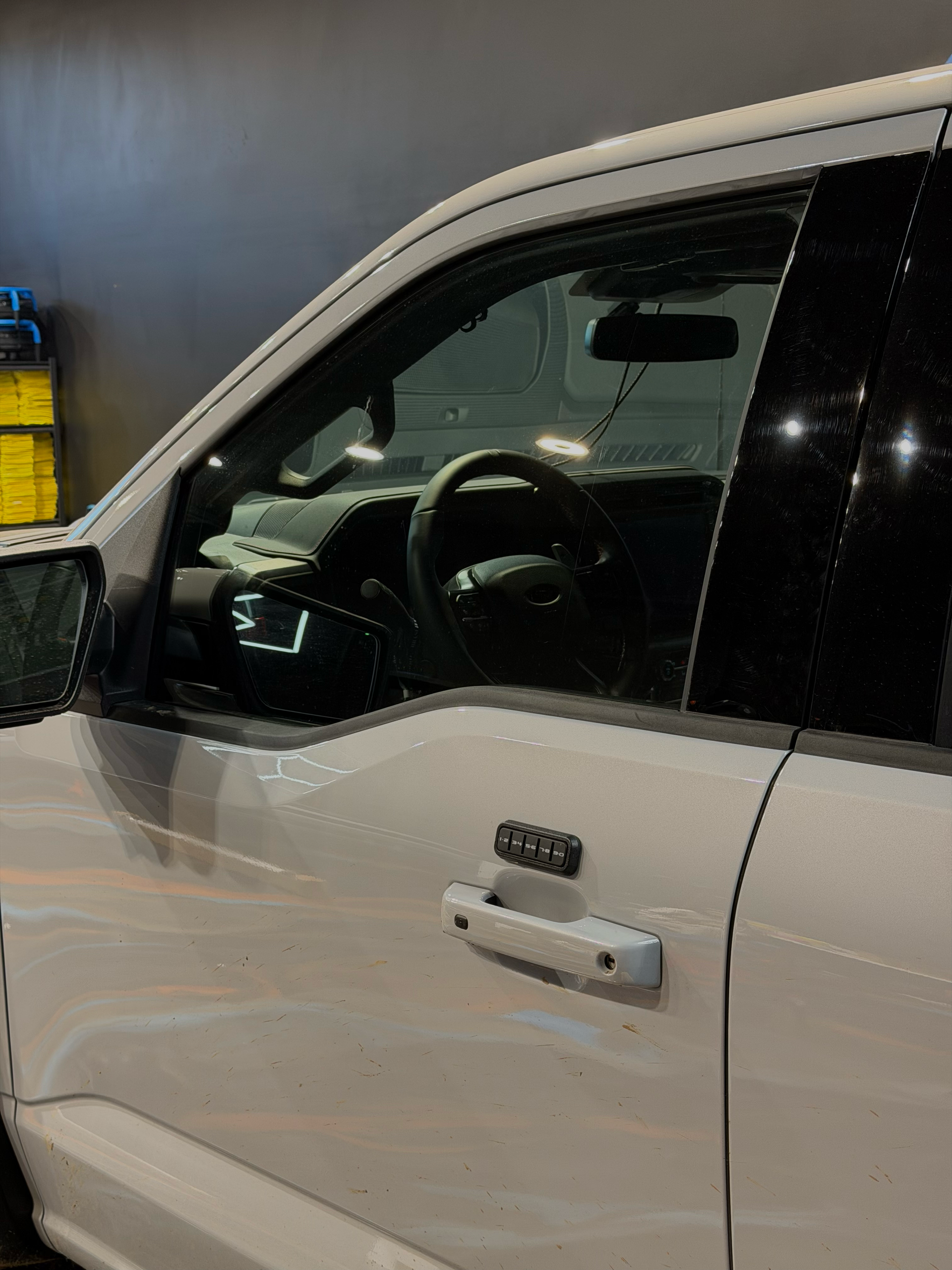 White Ford F-150 truck, parked indoors. Side view showing door handle and window, interior details visible.