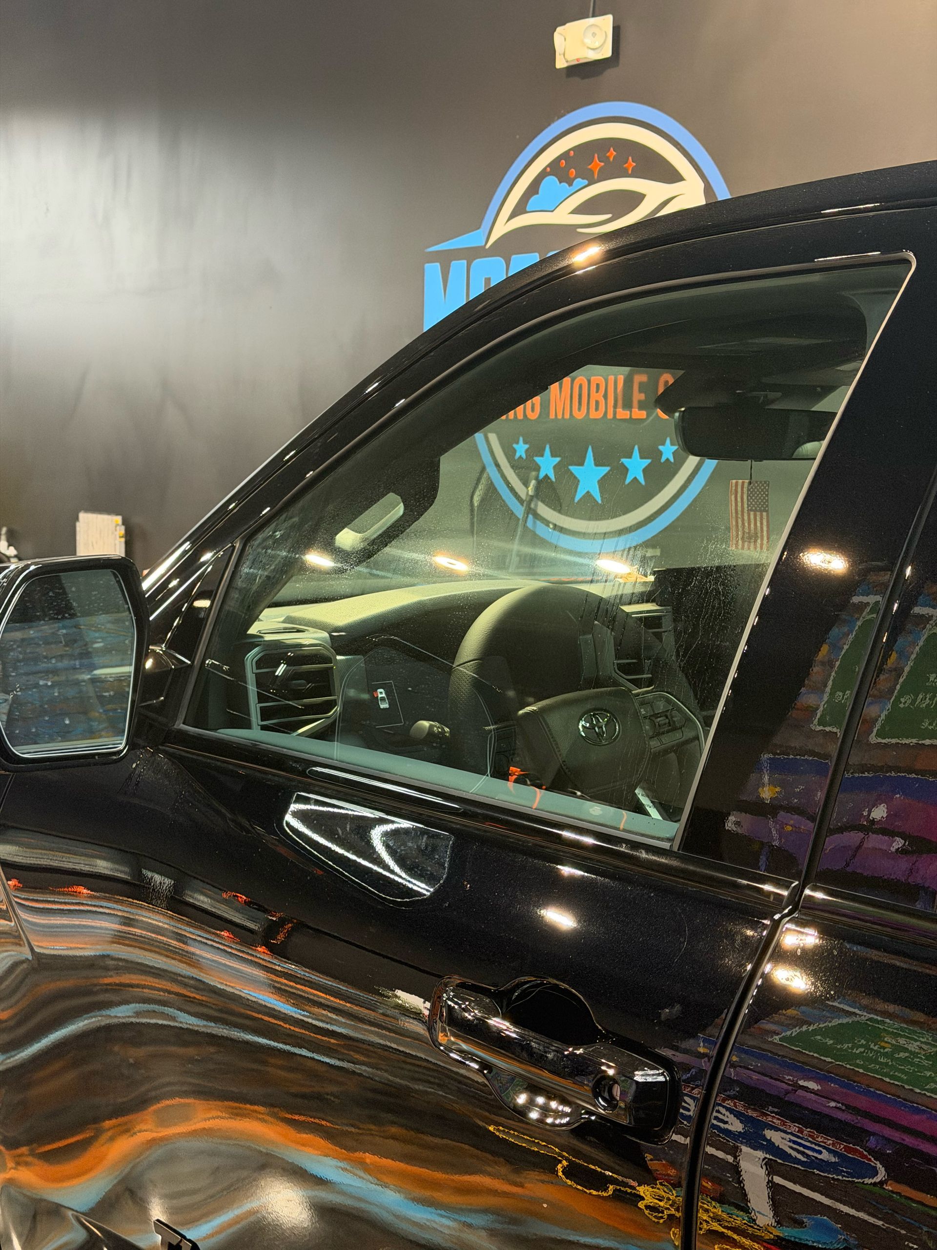 Black SUV close-up with tinted windows in a showroom or garage, reflecting colorful lights.