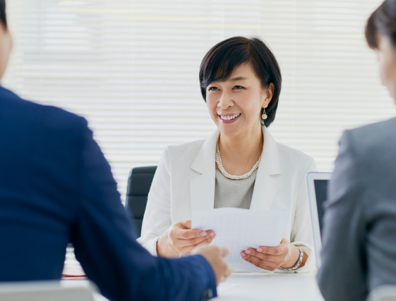 Business meeting with people exchanging papers, featuring a smiling person in a white blazer