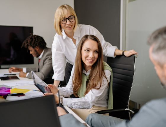 Colleagues in a meeting room, smiling around a laptop and documents at a conference table