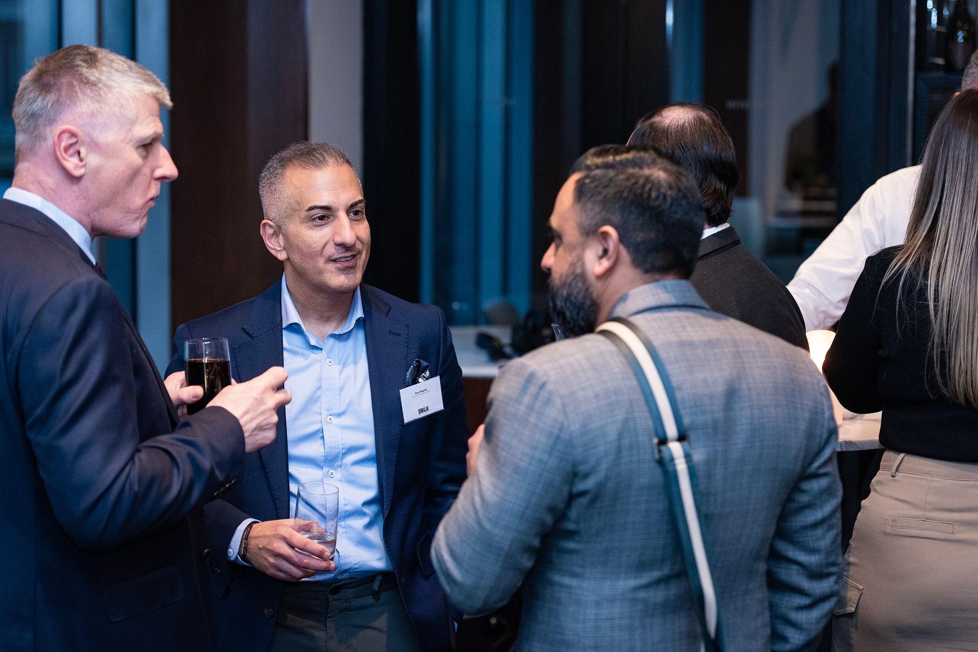 People networking at an indoor event, chatting in small groups with drinks in hand.