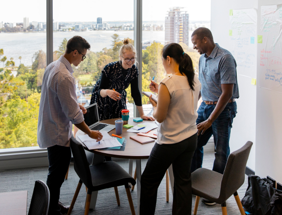 Team members gather around a table in a bright office, collaborating over papers and colorful materials.