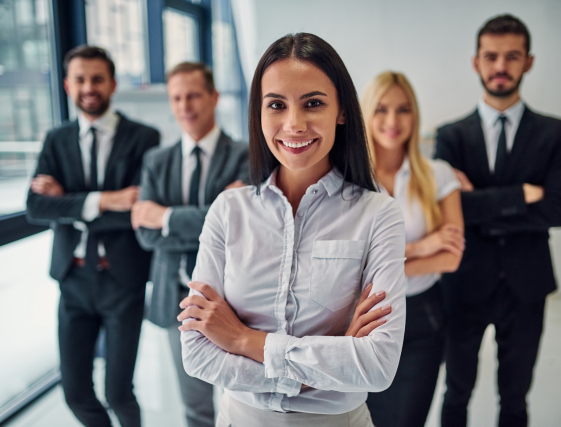 Business team standing together in an office, with a smiling woman in a white shirt in front.