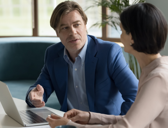 Two colleagues in a meeting, discussing beside a laptop in a bright office.