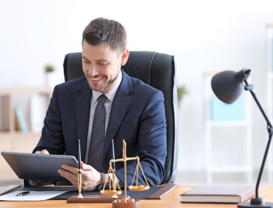 Lawyer in a suit reviewing a tablet at a desk with a scale of justice and lamp