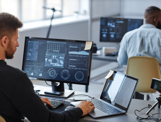 People working at computer desks in a modern office, with multiple monitors and laptops.