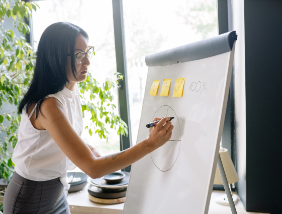 Woman writing on a flip chart with sticky notes in a bright office.