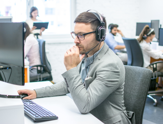 Man wearing headphones and glasses working at a desk in a busy office