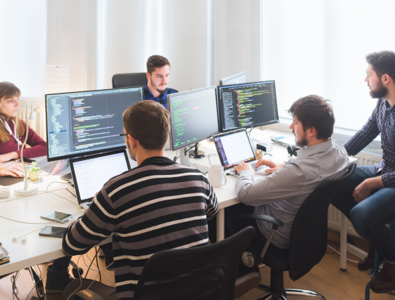 Team of developers collaborating around multiple computer monitors in an office meeting room