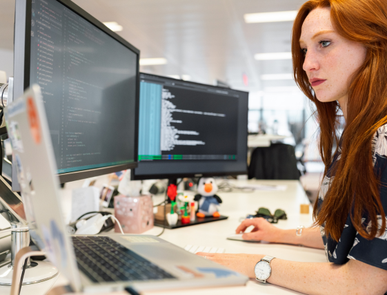 Person working at a desk with dual monitors in a bright office