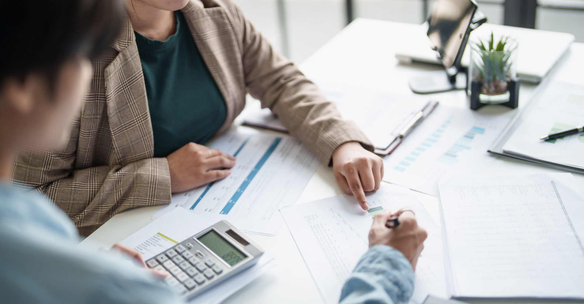 Two people reviewing financial charts at a desk with a calculator and documents.