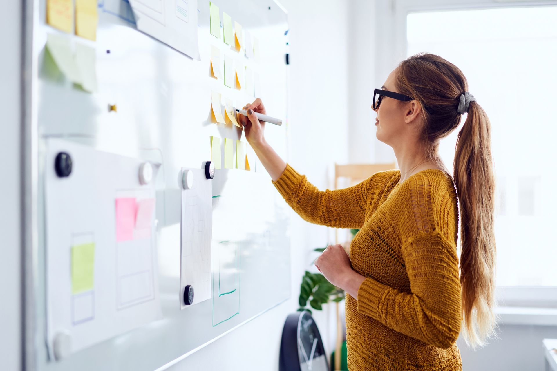 Woman in glasses writing on sticky notes on a white office wall board