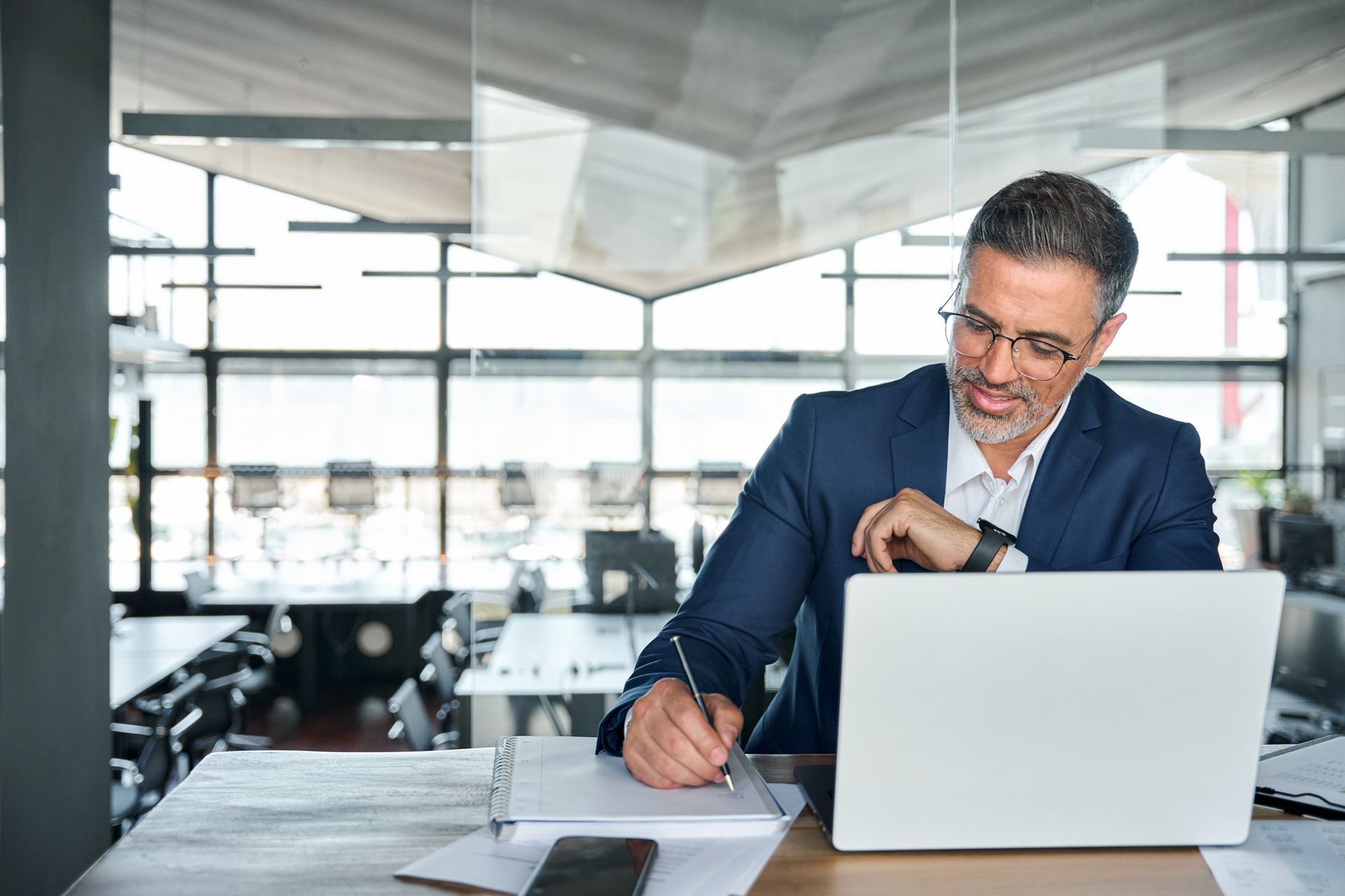 Man in a blue suit writing at a laptop in a modern office conference room