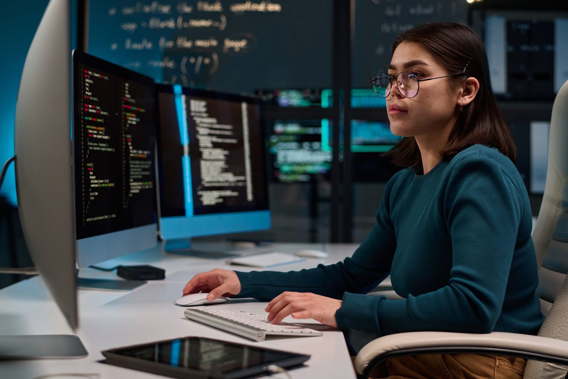 Person working at a desk with multiple monitors showing code in a modern office
