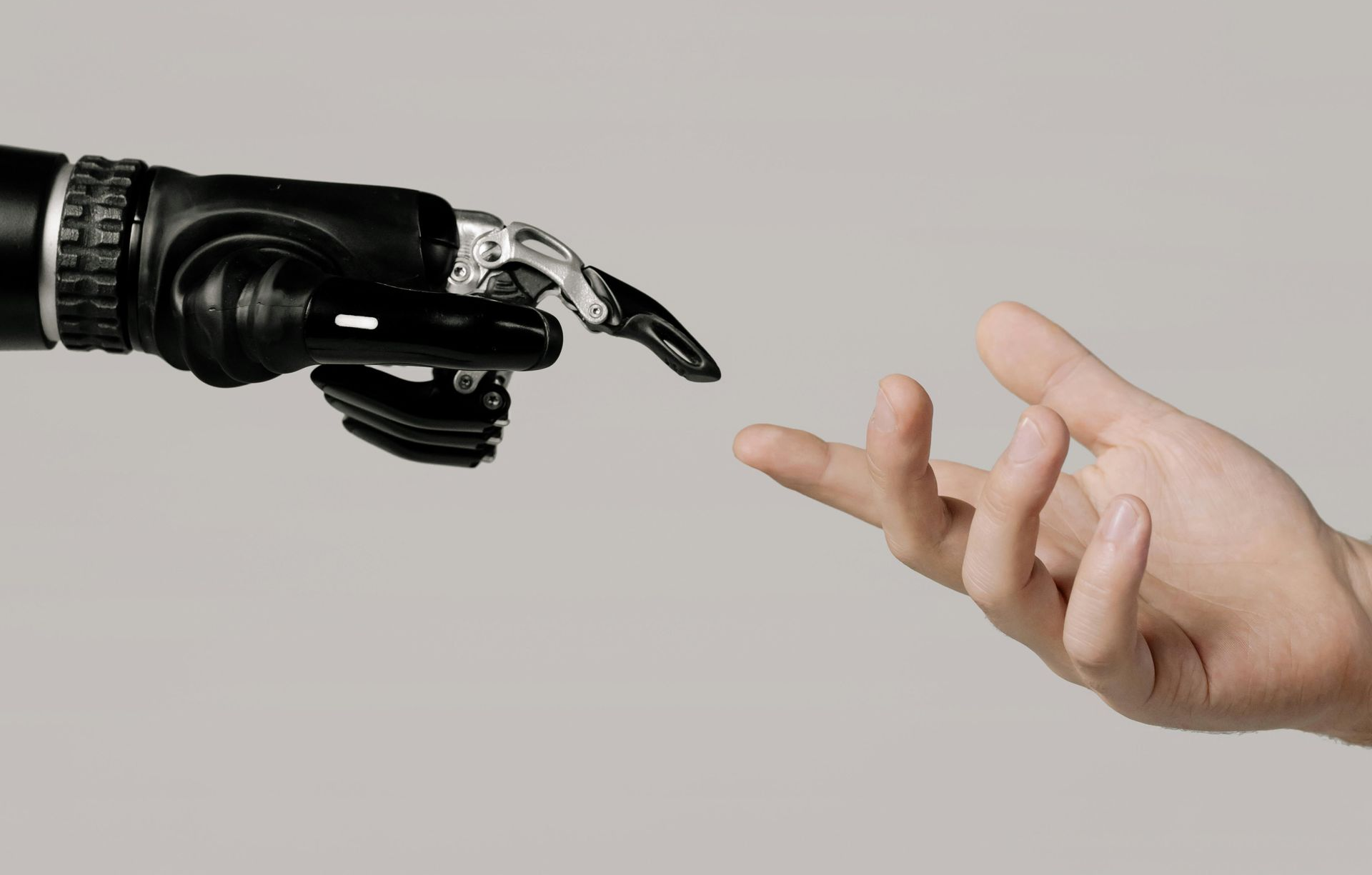 Robotic hand reaching toward a human hand against a plain gray background