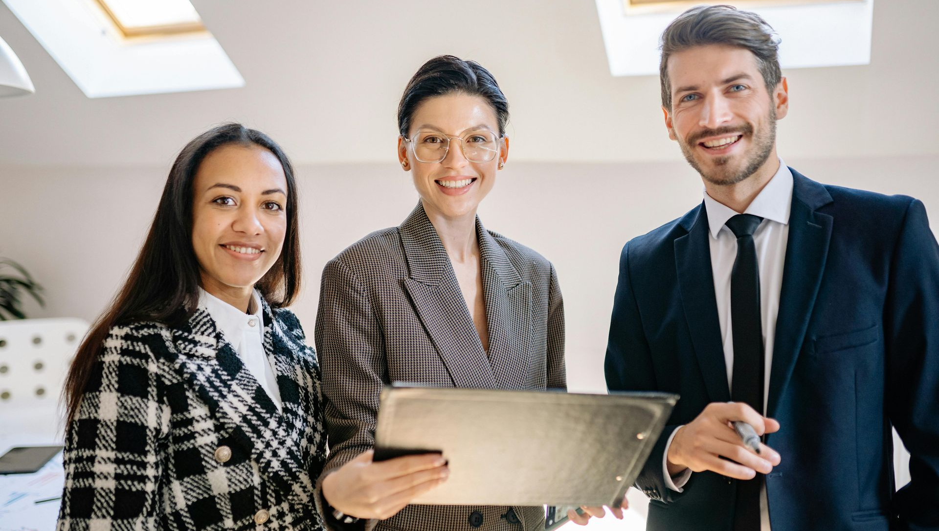 Three business professionals holding a folder and smiling in a bright office meeting room